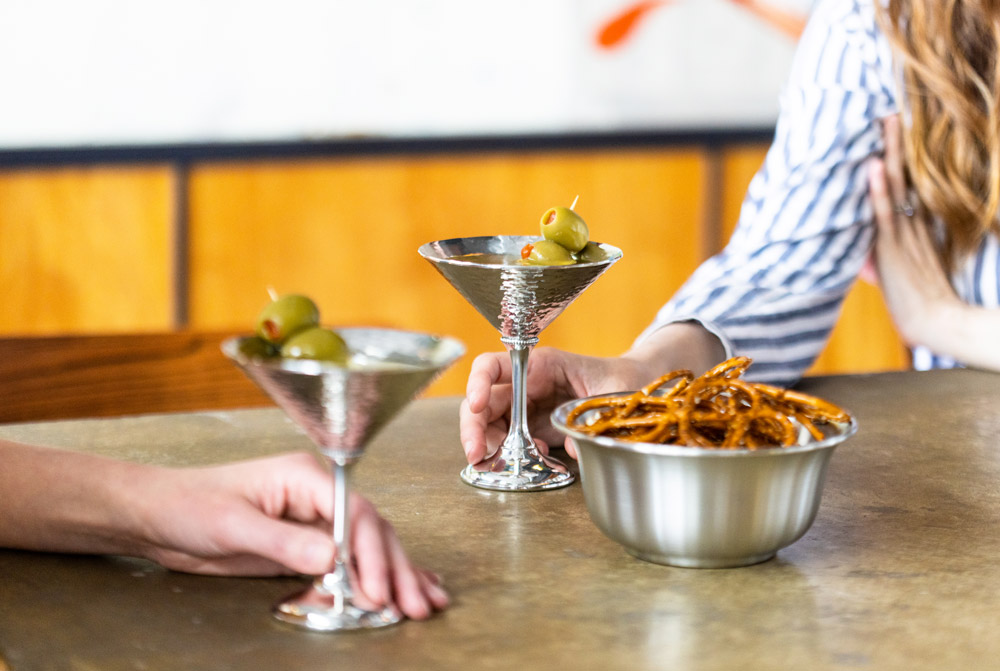 2 people drinking martinis with a bowl of pretzels