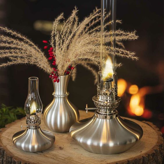 2 pewter oil lamps and a pewter vase in front of a fire