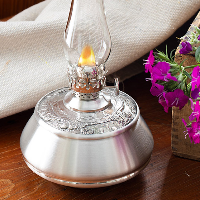 close up of pewter oil lamp showing countryside design