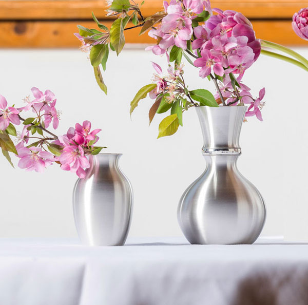 two pewter vases with pink flowers in them sitting on a table